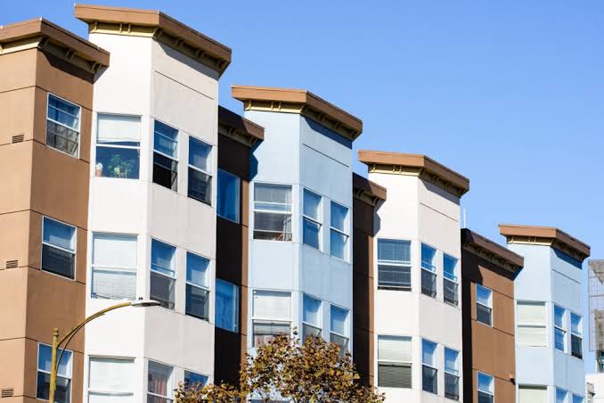 Exterior view of a modern multi-story residential building with brown, white, and blue facade panels, showcasing a well-maintained complex under professional Apartment Property Management.