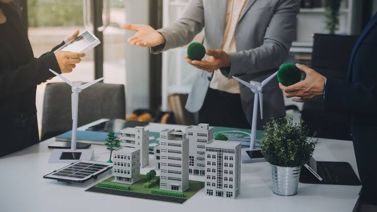 Professionals discussing sustainable energy solutions around architectural building models and miniature wind turbines for Residential Building Management.