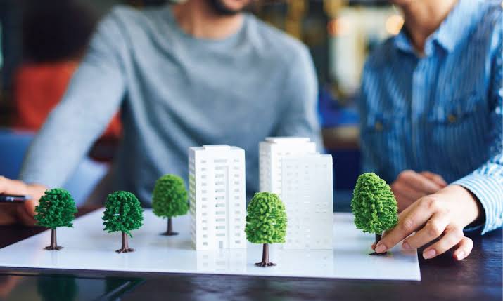 Two people arranging miniature trees around high-rise architectural models, highlighting sustainable Residential Building Management.