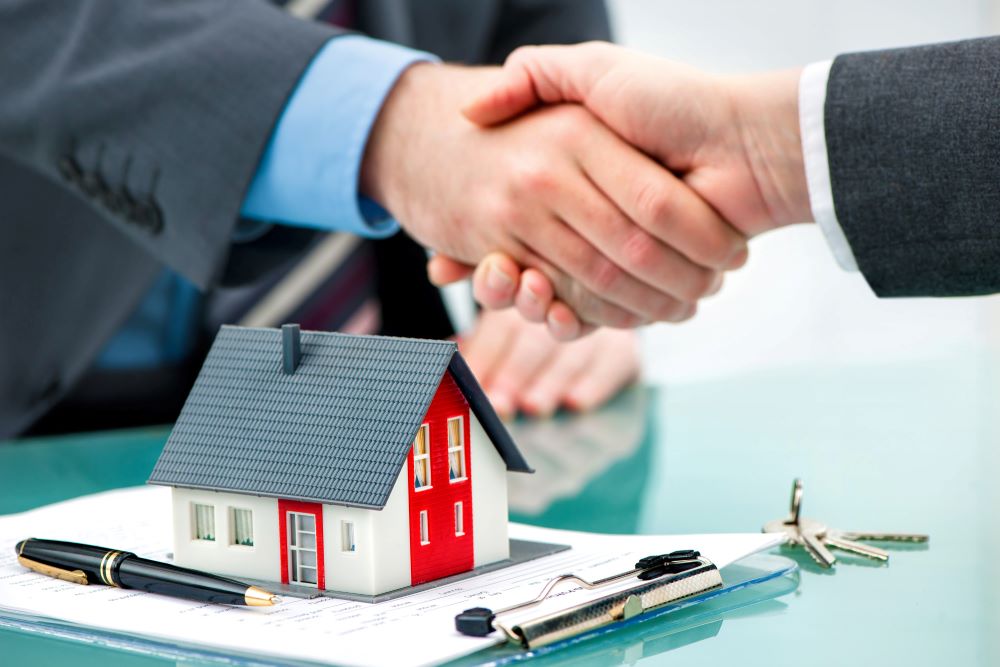 Two professionals shaking hands over a miniature house model and contract, representing Professional Property Management Services.