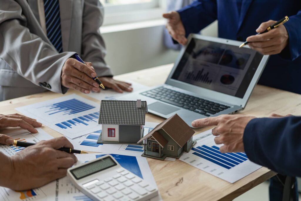 A real estate team analyzing financial reports and house models during a meeting for Professional Property Management Services.