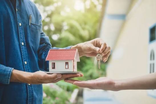 A property manager handing house keys to a client alongside a model home, representing Professional Property Management Services.