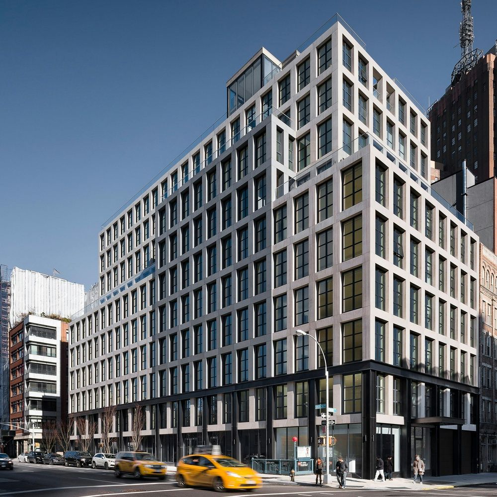 A low-angle view of a modern multi-story apartment building featuring a geometric grid facade with large windows, showcasing residential real estate maintained by a professional Property Management Company Queens.