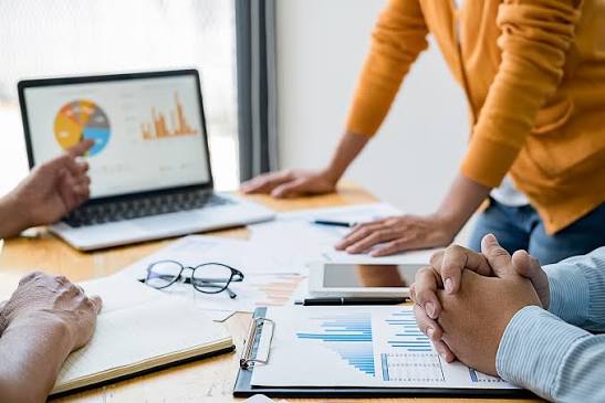 A business team analyzing performance pie charts and financial reports around a conference desk, illustrating tailored Property Management Consulting Services.