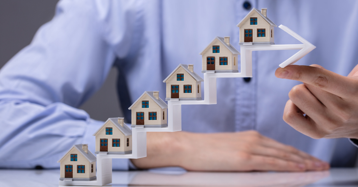 Hand lifting an ascending arrow lined with miniature house models, symbolizing real estate growth and portfolio expansion with a Rental Property Management Company.