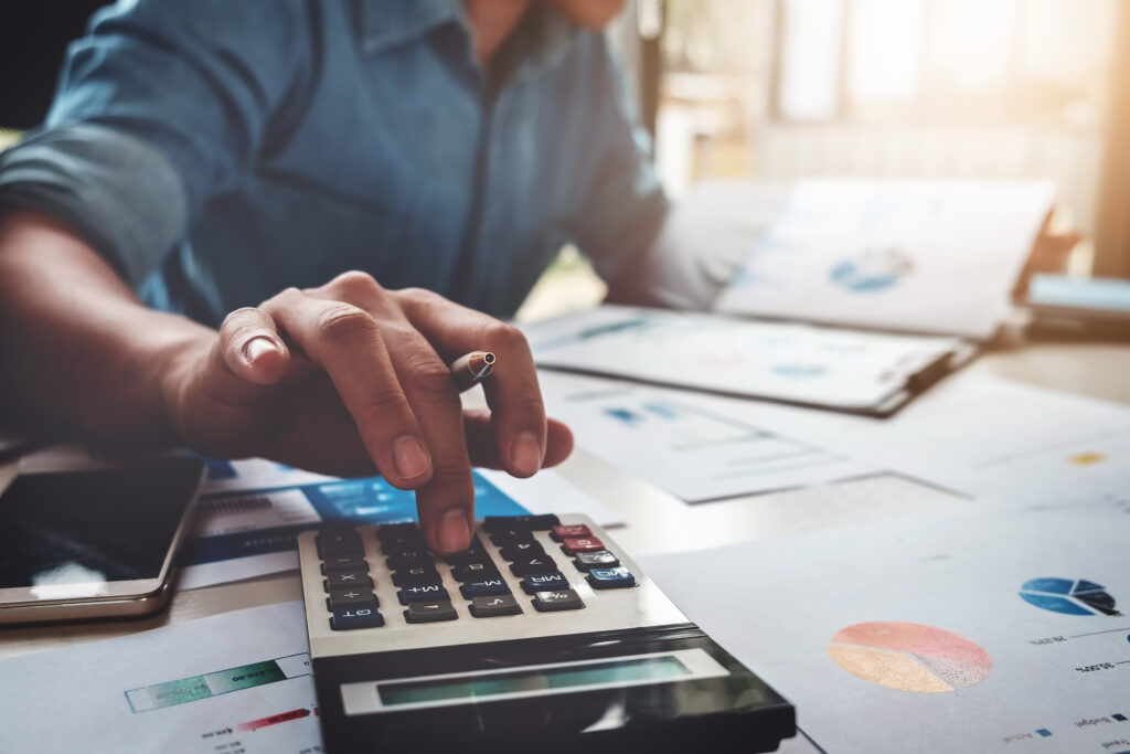 An accountant entering numbers into a desktop calculator while examining financial reports and pie charts during a Rental Property Accounting review.